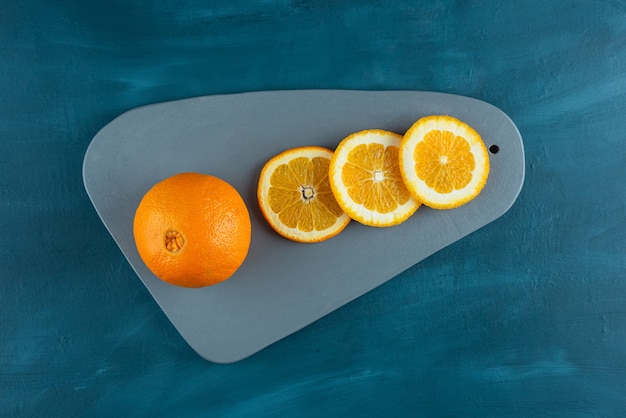 Ganze und in Scheiben geschnittene Orangenfrüchte auf einen dunkelblauen Tisch gelegt.