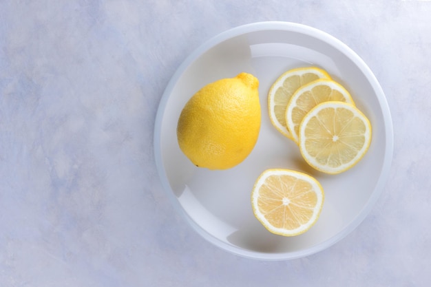 Ganze Zitrone und Zitronenscheiben auf einem weißen Teller Zusammensetzung von Zitrusfrüchten auf hellgrauem Hintergrund Tropische Bio-Früchte Zitrusfrüchte Vitamin C Nahaufnahme