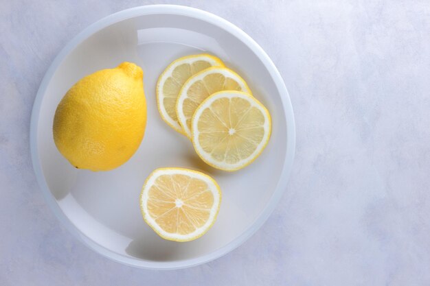 Ganze Zitrone und Zitronenscheiben auf einem weißen Teller Zusammensetzung von Zitrusfrüchten auf hellgrauem Hintergrund Tropische Bio-Früchte Zitrusfrüchte Vitamin C Nahaufnahme