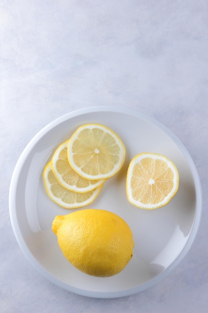 Ganze Zitrone und Zitronenscheiben auf einem weißen Teller Zusammensetzung von Zitrusfrüchten auf hellgrauem Hintergrund Tropische Bio-Früchte Zitrusfrüchte Vitamin C Nahaufnahme