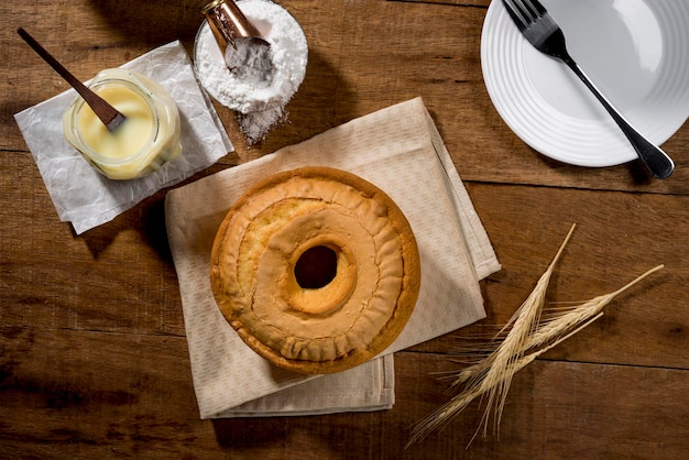 Ganzer Kuchen aus Kondensmilch auf Stoff und rustikalem Holz mit Topf mit Backpulver und Kuchen im Hintergrund. Ansicht von oben