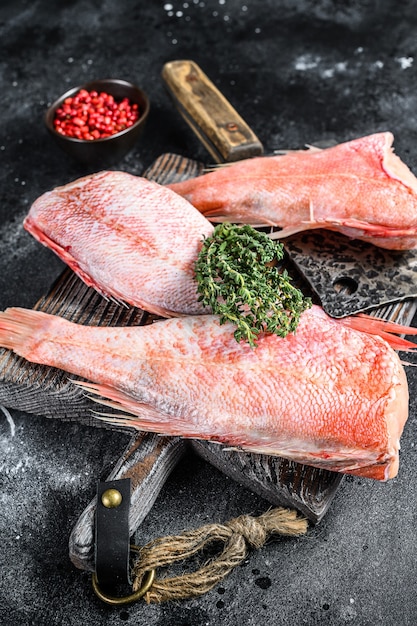 Ganzer roher Red Snapper Fisch auf einem Schneidebrett. Schwarzer Hintergrund. Draufsicht.