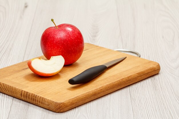 Ganzer roter Apfel und in Scheiben geschnitten mit Messer auf Holzbrett im grauen Hintergrund.