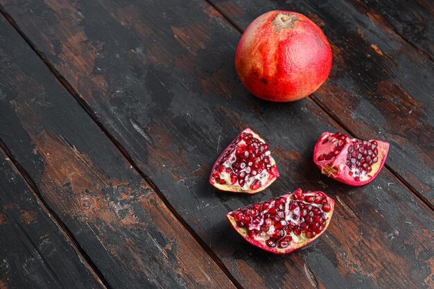 Ganzer und geschnittener Granatapfel über altem dunklem Holztisch, Seitenansicht mit Platz für Text.