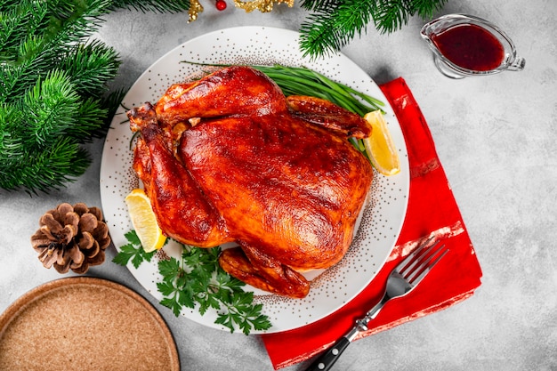 Ganzes gebackenes Hühnchen in Sauce mit Paprika auf einem Teller und einer weihnachtlichen Tischdekoration von oben. Foto in hoher Qualität