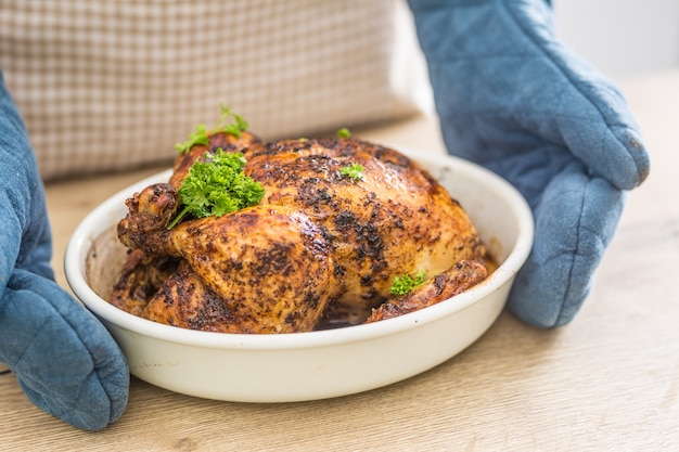 Ganzes gebratenes Huhn in einer Backschüssel, die in den Händen hält, kochen mit Handschuhen.