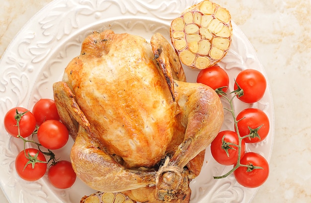 Ganzes gegrilltes Huhn auf einer Platte mit Tomaten und Knoblauch