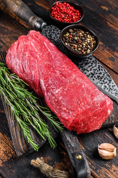 Ganzes rohes Rinderfilet für Steaks Filet Mignon auf einem Holzbrett mit Metzgermesser. Dunkler hölzerner Hintergrund. Ansicht von oben.