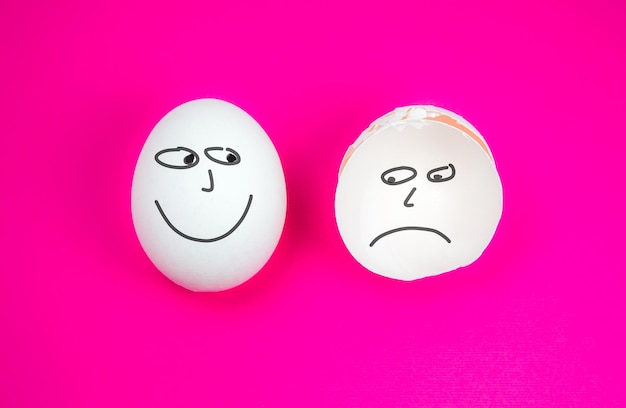 Ganzes weißes Ei mit Lächeln und zerbrochenes Ei mit trauriger oder negativer Emotion auf dem rosa Hintergrund Kopierbereich Minimalistisches, originelles und kreatives Foto Schöne Tapete Unterschiedliche Emotionen