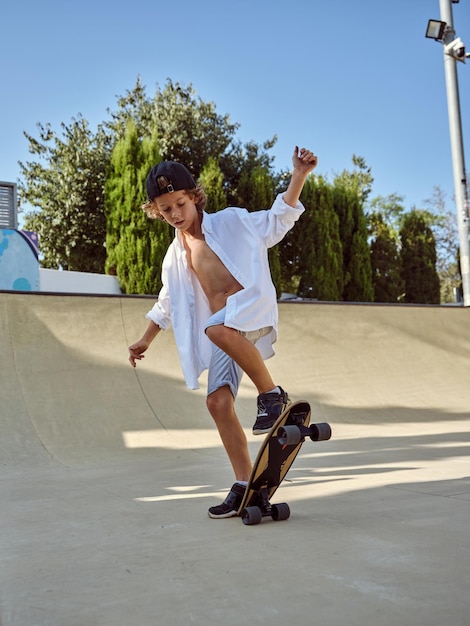 Ganzkörper-Seitenansicht eines jungen Skaters in Freizeitkleidung, der Skateboard auf der Straße balanciert und nach unten schaut, während er beim Skaten Tricks übt