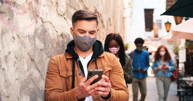 Ganzkörperansicht der gemischtrassigen Gesellschaft von Menschen, die Schutzmasken tragen, die mit jedem ...