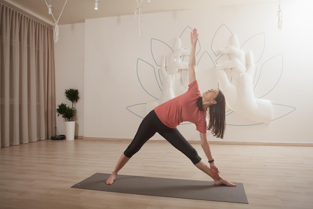 Ganzkörperaufnahme einer athletischen Frau, die Asana in Dreieckshaltung macht und Yoga praktiziert