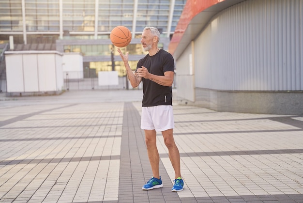 Ganzkörperaufnahme eines sportlichen reifen Mannes in Sportkleidung, der im Freien steht und mit Basketball spielt