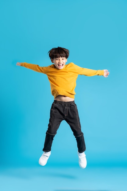 Ganzkörperbild eines asiatischen Jungen, der auf blauem Hintergrund posiert