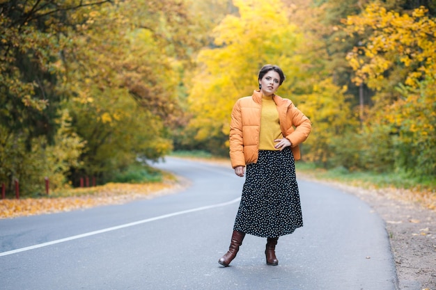 Ganzkörperfoto einer jungen Frau auf der Straße im Herbstwald, die an der frischen Luft spazieren geht und Freiheit und s genießt