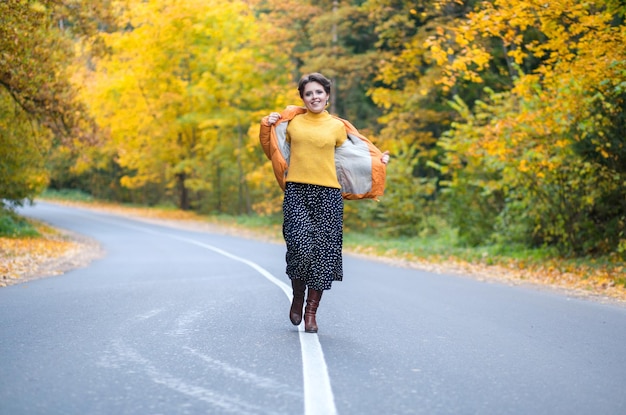 Ganzkörperfoto einer jungen Frau auf der Straße im Herbstwald, die an der frischen Luft spazieren geht und Freiheit und s genießt