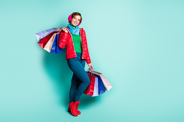 Ganzkörperfoto von positiven Mädchen Touristen halten viele Taschen, die sie am Herbst Herbst Wochenende tragen tragen grüne Pullover rote Saison tragen Schuhe rosa blaue Hosen Hosen isoliert türkisfarbene Wand