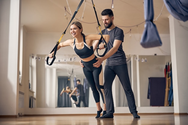 Ganzkörperporträt einer fröhlichen Dame, die den TRX-Suspensionstrainer während des Krafttrainings nutzt