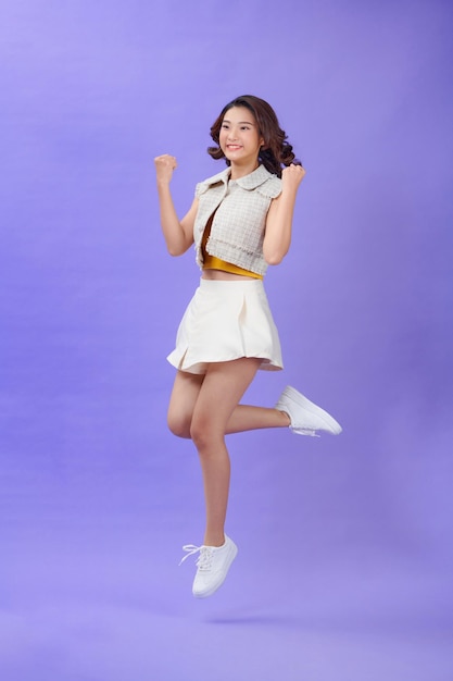 Ganzkörperporträt einer fröhlichen jungen asiatischen Frau, die Erfolg feiert, während sie isoliert über violettem Hintergrund springt