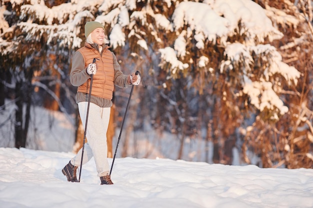 Ganzkörperporträt einer sportlichen Seniorin, die im Winterwald im Spa bei Sonnenuntergang spazieren geht