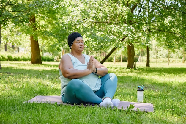 Ganzkörperporträt einer übergewichtigen schwarzen Frau, die im Freien Yoga macht und mit geschlossenen Augen i meditiert