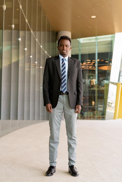 Ganzkörperporträt eines afrikanischen Geschäftsmannes mit Anzug und Krawatte im Freien in der Stadt