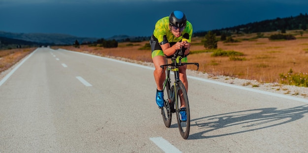 Ganzkörperporträt eines aktiven Triathleten in Sportbekleidung und mit Schutzhelm auf dem Fahrrad. Selektiver Fokus.