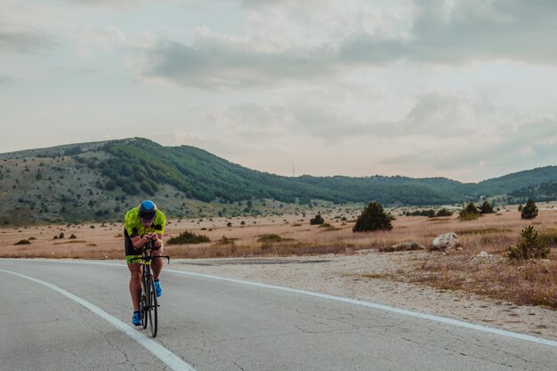 Ganzkörperporträt eines aktiven Triathleten in Sportbekleidung und mit Schutzhelm auf dem Fahrrad. Selektiver Fokus.