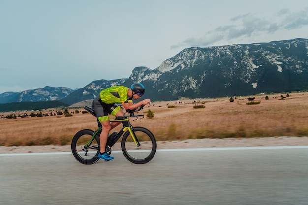 Ganzkörperporträt eines aktiven Triathleten in Sportbekleidung und mit Schutzhelm auf dem Fahrrad. Selektiver Fokus.