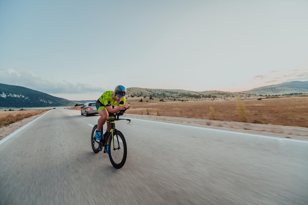 Ganzkörperporträt eines aktiven Triathleten in Sportbekleidung und mit Schutzhelm auf dem Fahrrad. Selektiver Fokus.