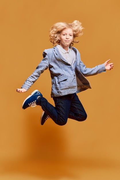 Ganzkörperporträt eines kleinen Jungen in Jacke, der vor orangefarbenem Studiohintergrund posiert