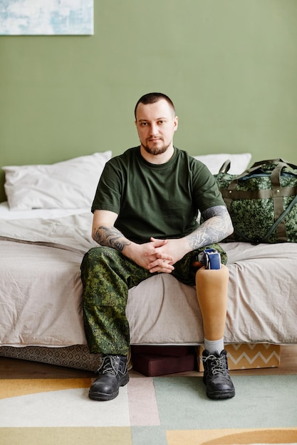 Ganzkörperporträt eines Militärveteranen mit Beinprothese, der zu Hause die Kamera anschaut und a