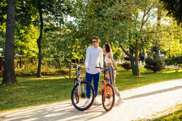 Ganzkörperporträt eines schönen jungen Mannes und einer Frau, die mit Fahrrädern im Park stehen