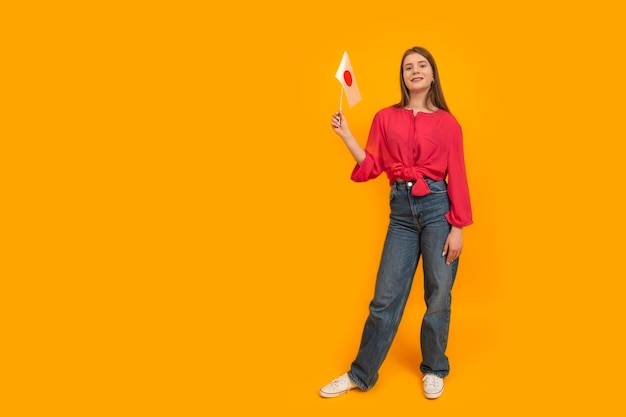 Ganzkörperporträt eines Teenager-Mädchens mit der Flagge Japans auf orangefarbenem Hintergrund Japanisch lernen Lernen Sie und reisen Sie nach Japan Platz für Text