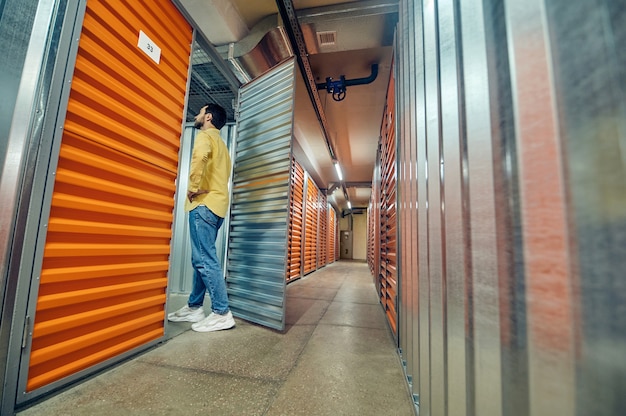 Garagem, entrada. Homem interessado em roupas casuais entrando pela porta aberta da garagem em um armazém moderno iluminado