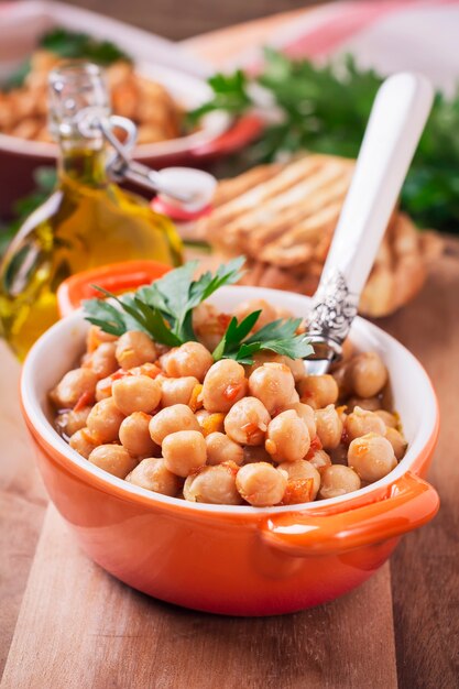 Garbanzos cocidos vegetarianos con tomate y perejil sobre superficie de madera vieja. Enfoque selectivo.