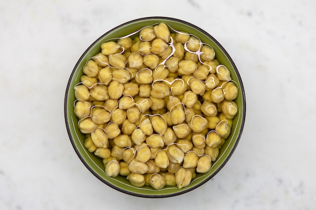 Garbanzos empapados en agua, en cuenco, sobre mesa de mármol. Concepto de alimentación saludable, veganismo, vegetarianismo, reemplazo de carne y huevo. Prepare los garbanzos antes de hacer hummus y otros platos de legumbres.