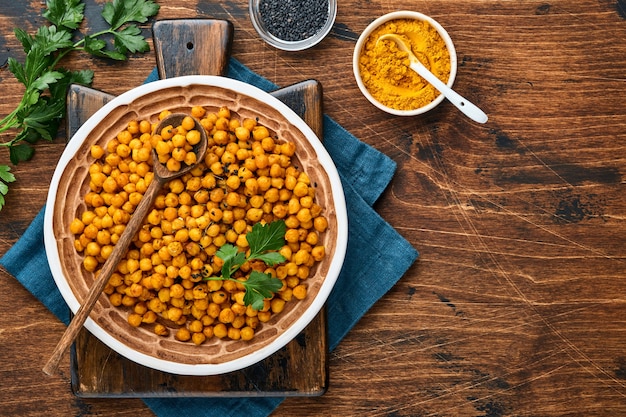 Garbanzos fritos con cúrcuma en plato de cerámica sobre un fondo de mesa de madera vieja. Garbanzos picantes asados o chana o chole de la India, receta popular de bocadillos. Vista superior.