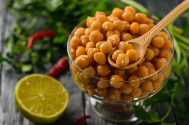 Garbanzos hervidos en un bol de vidrio, pimienta y limón sobre una mesa. Cocina vegetariana a partir de legumbres.