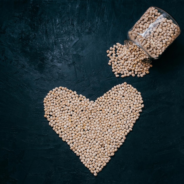 Garbanzos o garbanzos secos saludables derramados de un tarro de vidrio en forma de corazón frijoles crudos orgánicos aislados sobre fondo negro Alimentos vivos y bienestar