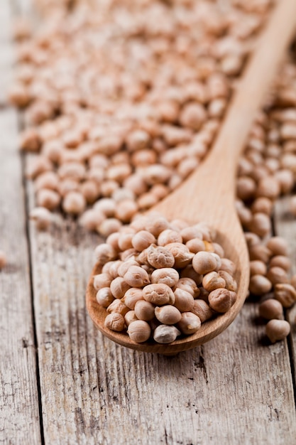 Garbanzos orgánicos crudos frescos en cuchara de madera en la tabla de madera rústica