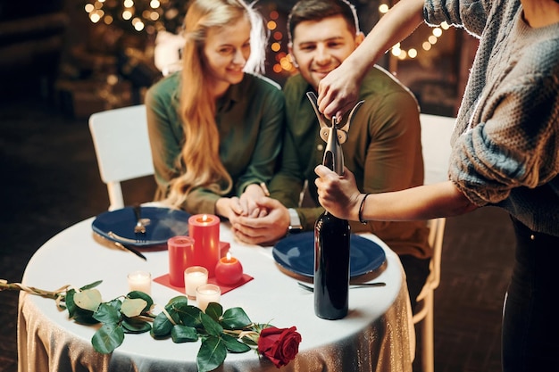 Garçom abre bebida de vinho Jovem casal adorável tem jantar romântico dentro de casa juntos