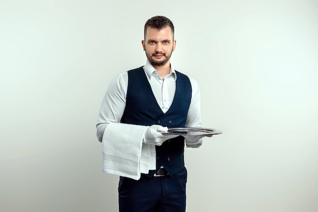 Garçom bonito, de camisa branca, segurando uma bandeja de prata. o conceito de servir o pessoal que atende os clientes em um restaurante.