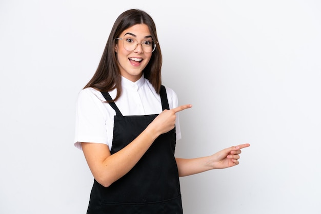 Garçom brasileiro de restaurante isolado no fundo branco surpreso e apontando o lado