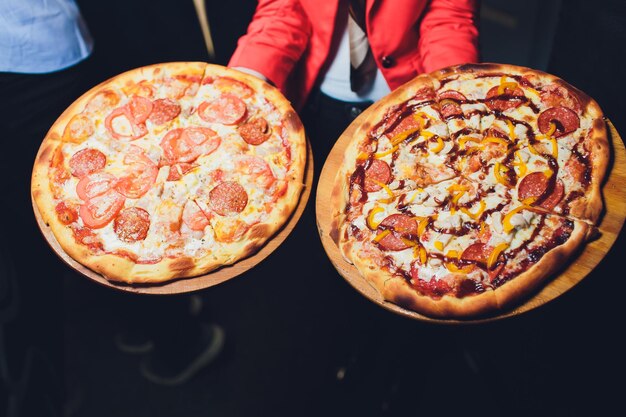 Foto garçom carregando dois pratos diferentes com uma pizza saborosa foto com duas pizzas pizza com cogumelos e pizza com salame comida italiana restaurante italiano