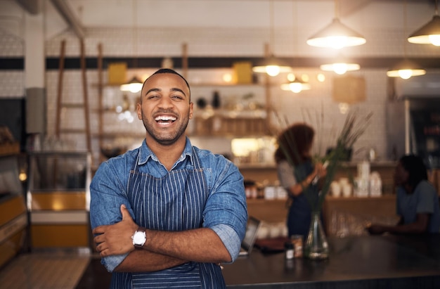 Garçom de cafeteria e retrato de homem negro riem no restaurante para serviço de café trabalhando e braços cruzados Inicialização de bistrô de pequeno empresário e barista masculino feliz na cafeteria pronto para servir