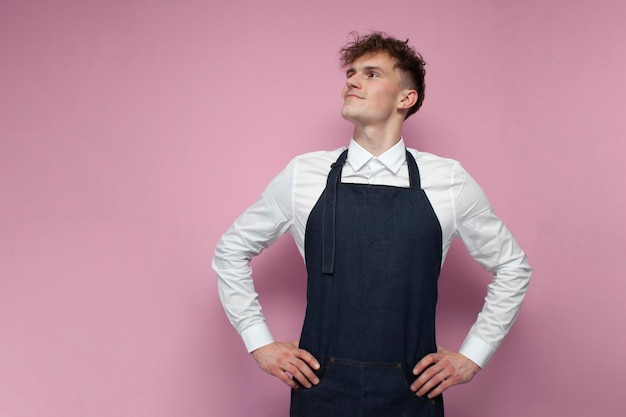 Garçom de camisa branca e avental sorrindo em fundo rosa retrato cara encaracolado trabalhador barista