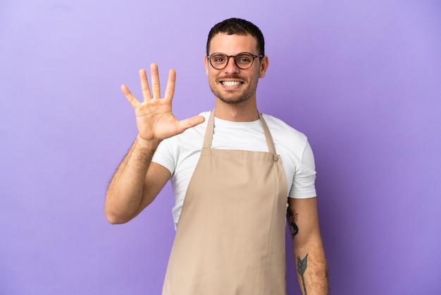 Garçom de restaurante brasileiro em fundo roxo isolado contando cinco com os dedos