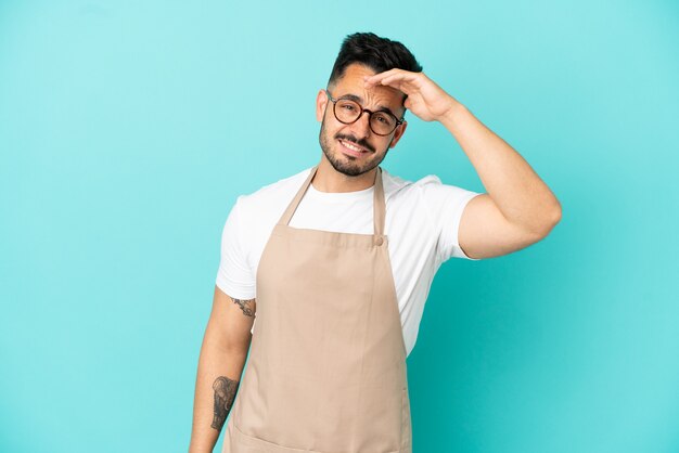 Garçom de restaurante homem caucasiano isolado em um fundo azul olhando para longe com a mão para olhar algo