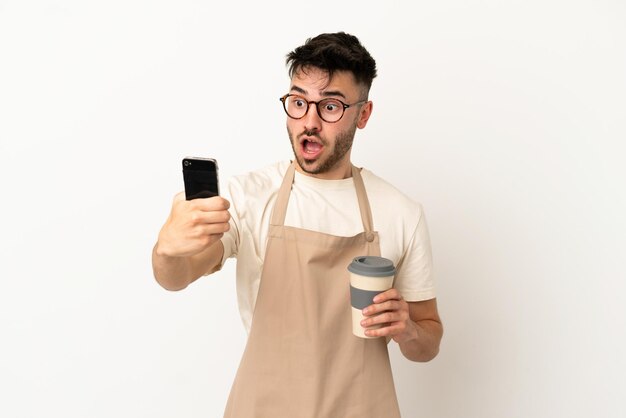 Garçom de restaurante, homem caucasiano, isolado no fundo branco, segurando um café para levar e um celular